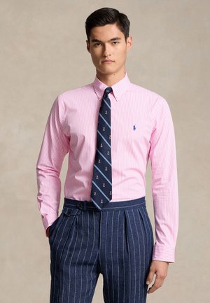 Chemise rayée rose à boutons, avec une cravate marine ornée de motifs d'ancre, assortie à un pantalon bleu à fines rayures.