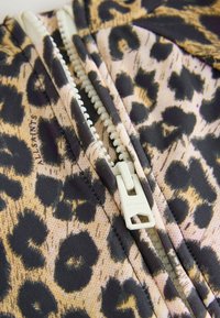 Tissu à imprimé léopard avec des motifs noirs et fauves, doté d'une fermeture éclair blanche au centre. Des coutures détaillées sont visibles le long des coutures.
