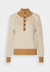 Kremowy sweter z dzianiny z brązowymi ściągaczami przy kołnierzu, mankietach i dolnej krawędzi, z pięcioma guziczkami w kolorze muszli żółwia z przodu.