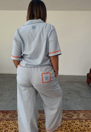 Striped pajama set in blue and white with orange trim. Features a collared shirt and wide-legged pants, with a square pocket on the back.
