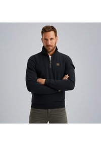 Crna polar jakna na zip s visokim ovratom, sa malim logom na prsima i rebrastim manžetama. Strukturalno prilagođen kroj, mekani materijal.