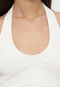 Gros plan d'une personne portant un haut dos-nu côtelé blanc, montrant le cou, les clavicules et le haut de la poitrine.