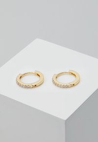 Goldene Creolen mit glatter Oberfläche, die eine Reihe kleiner klarer Edelsteine an einer Seite aufweisen. Kreisförmige Form mit einem Schnappverschluss.