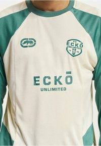 Krém színű, hosszú ujjú póló türkizkék részletekkel. A mellkasán "ECKŌ UNLIMITED" felirat és logó található. Simó, könnyű anyagból készült.