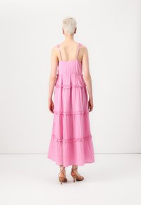 Pink, tiered maxi dress made of crinkled fabric with floral straps. Features ruffle accents along seams and a flowy silhouette.