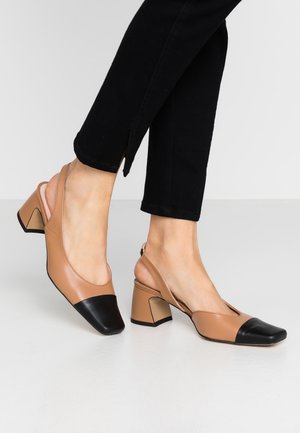 Braune Leder Slingback-Schuhe mit einer schwarzen Zehenkappe. Quadratische Zehen, klobige Absätze und eine glatte Textur. Getragen mit schwarzen Cropped-Hosen.