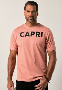 Kortærmet, pink t-shirt lavet af blødt stof med "CAPRI" i fede sorte bogstaver tværs over brystet. Minimalistisk design, rund halsudskæring.