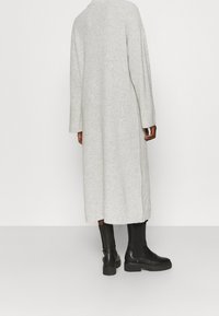 Cardigan lungo grigio in maglia con spalle basse, texture a costine, lati spaccati e colletto alto. Abbinato a stivaletti neri alla caviglia.