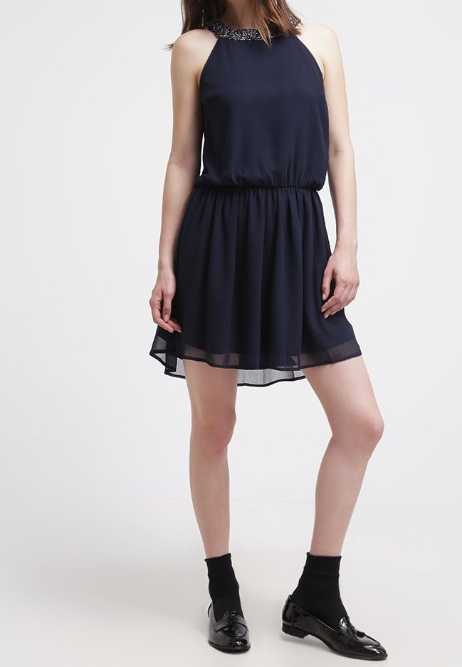 Marinblå ärmlös klänning med insydd midja, genomskinlig nederkant och detalj med pärlor i halsringningen. Bärs med svarta strumpor och skor i lackskinn.