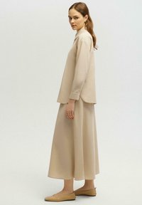 Chemise beige à manches longues, coupe décontractée avec un col, associée à une jupe longueur cheville assortie. Design simple et texture de tissu douce.