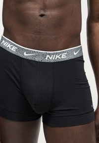 Ανδρικός κορμός που φοράει μαύρα εσώρουχα Nike boxer με γκρι ζωνάκι με σχέδιο, με λευκά λογότυπα Nike και σύμβολα swoosh.