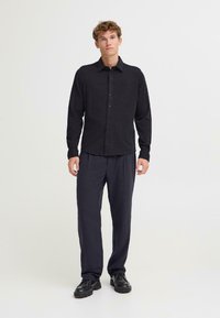 Camicetta nera con bottoni, dalla texture morbida, maniche lunghe, abbinata a pantaloni navy larghi e scarpe nere. Design semplice e funzionale.