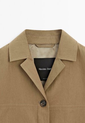 Khakifarbene Jacke mit spitzem Kragen, ausgestattet mit einem einzelnen Knopfverschluss und sichtbaren Nähten. Mit dem Etikett "Massimo Dutti" im Inneren.