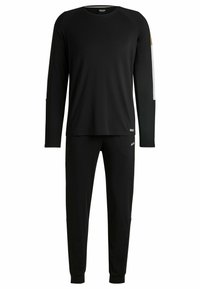 Haut à manches longues noir et pantalon assorti en tissu doux. Le haut présente des rayures contrastantes, des détails de logo sur les deux articles et des poignets côtelés.
