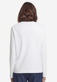 Witte lange mouwen shirt gemaakt van katoen, met een eenvoudige ronde hals en een relaxte pasvorm, gedragen met donkerblauwe spijkerbroek.