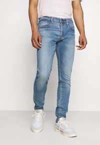 Jean en denim bleu clair à coupe slim, doté d'un design classique à cinq poches et d'un léger effet délavé. Associé à des baskets blanches.