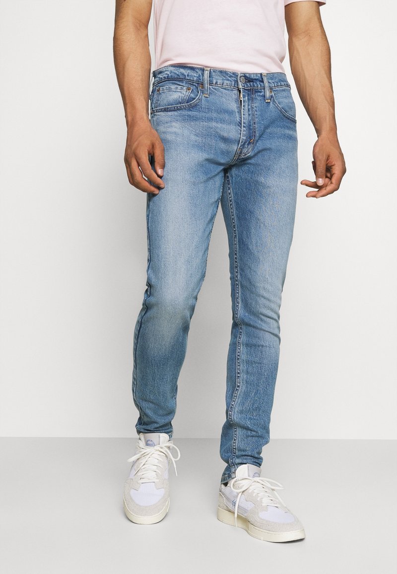 Jean en denim bleu clair à coupe slim, doté d'un design classique à cinq poches et d'un léger effet délavé. Associé à des baskets blanches.