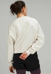  lichtbeige cropped sweatshirt met een relaxed fit, geribde boorden en een gestikte yoke. Gepaard met zwarte shorts voor een casual look.