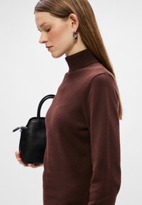 Sudadera de cuello alto marrón con textura acanalada, diseño ajustado y sutil adorno. Complementada con un pequeño bolso negro.
