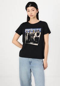 T-shirt en coton noir avec un motif vintage des Backstreet Boys en bleu et noir. Manches courtes et coupe décontractée. Associé à un jean bleu clair.