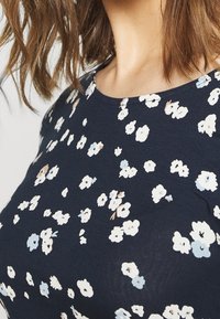 Marinblus med blommönster som har vita, ljusblå och beiga blommor. Rund halsringning och mjuk tygtextur.