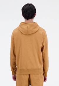 Sudadera con capucha en color mostaza, hecha de tela suave, cuenta con puños y dobladillo acanalados, con un corte relajado y diseño de bolsillo canguro.