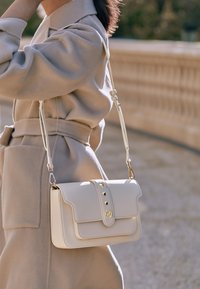Borsa a tracolla bianca in pelle con pattina, hardware dorato, tre borchie decorative e finitura strutturata. Tracolla regolabile e design strutturato.