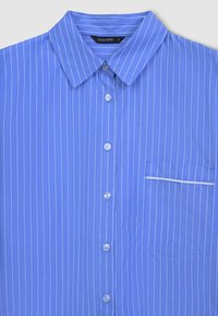 Chemise bleu à boutons avec des rayures blanches verticales, un col classique et une poche dotée d'une bordure blanche. Le tissu est lisse et léger.