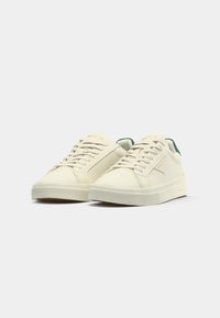 Cream-colored sneakers with green accents, featuring a smooth leather upper, textured rubber sole, and six eyelet lace closure.