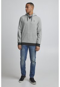 Gray hoodie with a drawstring and kangaroo pocket, black cuffs and hem, paired with blue jeans and black sneakers. Simple, casual design.