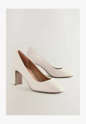 Białe skórzane szpilki z ostro zakończonym noskiem i masywnym obcasem. Teksturowana powierzchnia z gładkim wnętrzem.