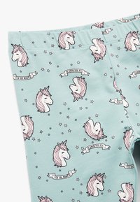 Leggings hechos de una suave tela azul claro con un estampado de unicornios, crines rosas y el texto "ERES MÁGICO" en una bandera blanca con estrellas.