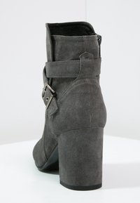 Graue Wildleder-Stiefelette mit Blockabsatz, seitlichem Reißverschluss und dekorativem Riemen mit Schnalle um den Knöchel.