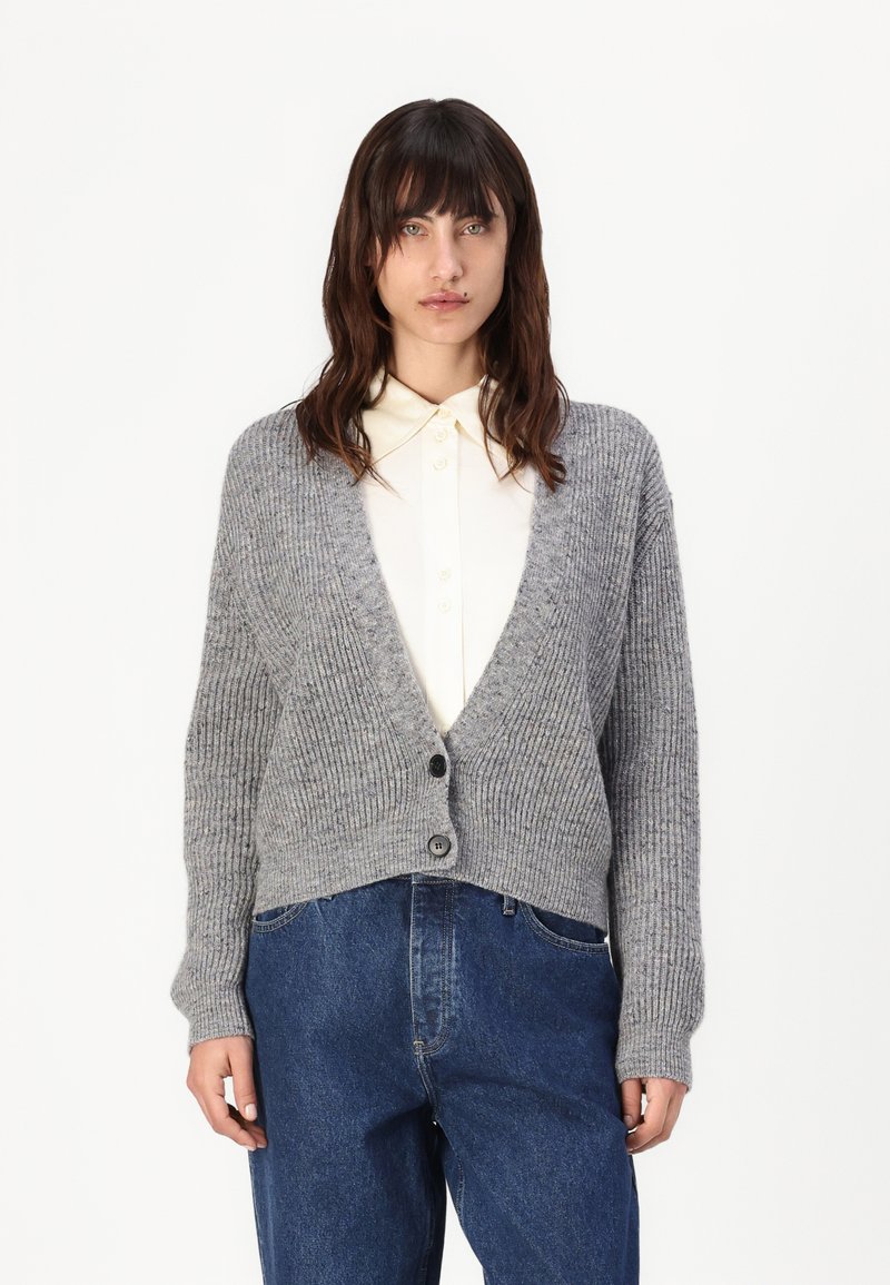Cardigan grigio a coste con scollatura a V profonda, due bottoni frontali e maniche lunghe. Abbinato a una camicia colletto di colore chiaro e pantaloni in denim.