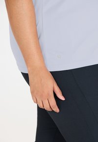 Lyseblå træningstop med korte ærmer og et subtilt logo, parret med sorte tætsiddende leggings. Glat stof uden synlige mønstre.