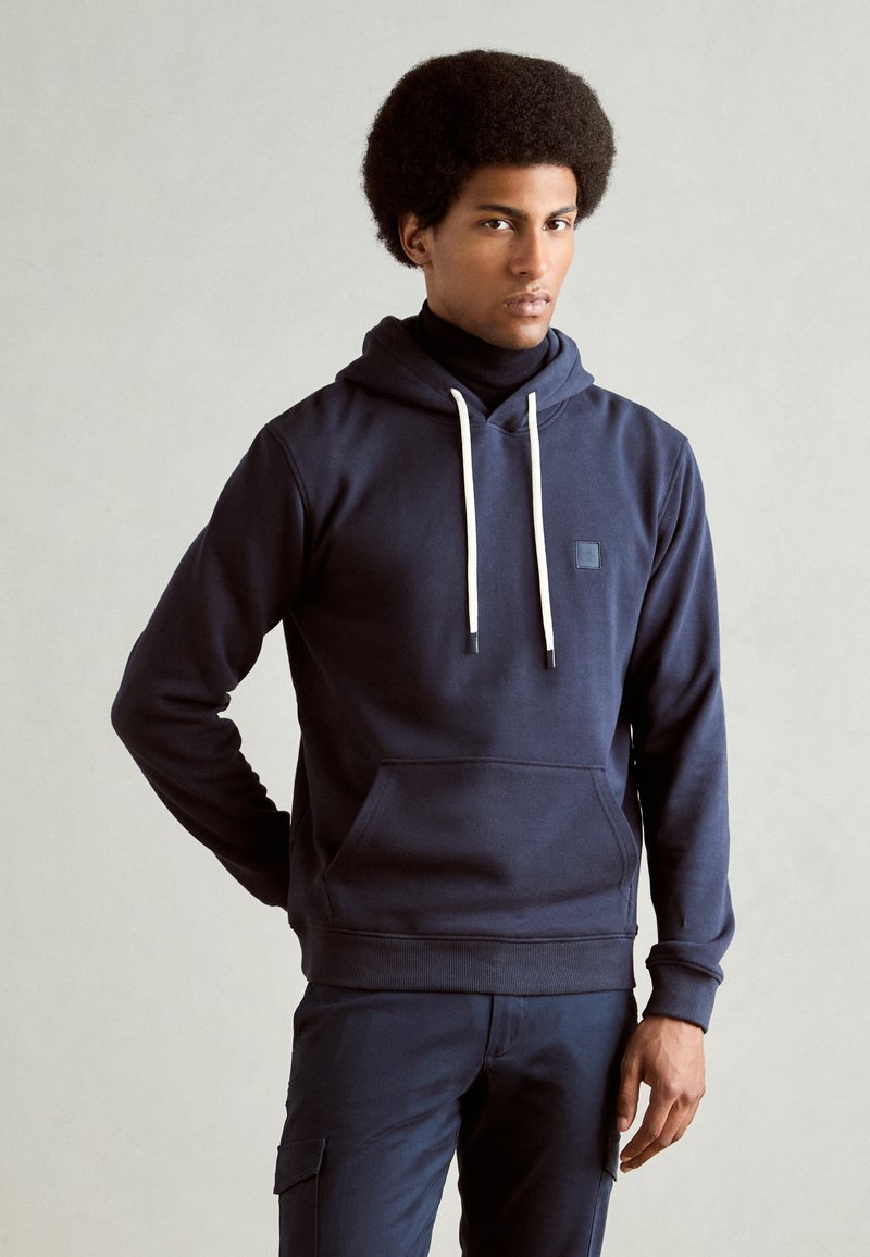 Sudadera azul marino de mezcla de algodón, con un bolsillo frontal, cordones blancos y un pequeño parche con el logotipo en el pecho.