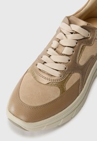 Baskets en cuir beige avec daim texturé, lacets crème et accents dorés métalliques. Bout arrondi et semelle rembourrée pour le confort.