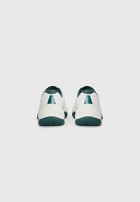 Pantofi sport albi cu o talpă verde texturată, având accente verzi la călcâi și spate, și un material superior sintetic neted.