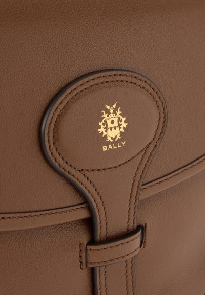 Καφέ δερμάτινη τσάντα με μαλακή υφή. Διαθέτει χρυσό λογότυπο και λεπτομερείς ραφές. Το κλείσιμο έχει στρογγυλεμένη διακοσμητική πινελιά.