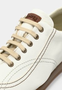 Λευκό δερμάτινο αθλητικό παπούτσι με μπεζ κορδόνια, μπρονζέ χάντρες και καφέ δερμάτινη λεπτομέρεια στη γλώσσα· διαθέτει διακριτικές ραφές.