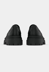 Black leather platform sneakers with a smooth finish, rounded shape, thick rubber soles, and textured tread for grip.