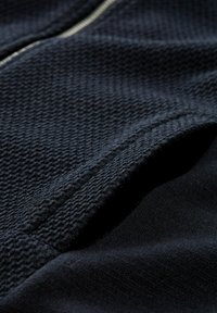 Close-up of dark blue textured fabric with a visible zipper and a layered fold showing different knit patterns.