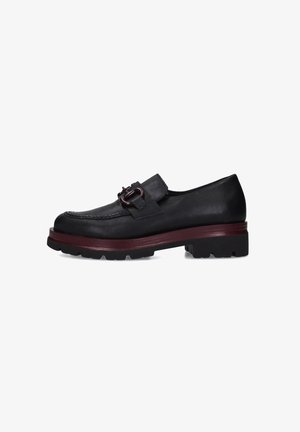 Scarpa in pelle nera con finitura texture, caratterizzata da un accento bordeaux sulla suola e un dettaglio a fibbia sulla tomaia. Design con suola spessa.