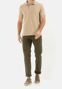 Beżowa koszulka polo z kołnierzykiem, khaki spodnie i beżowe sneakersy. Koszulka polo ma małe logo i jest wykonana z miękkiego, teksturowanego materiału.