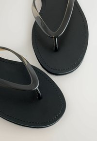 Sorte klipklapper med en glat gummisål og gennemsigtige stropper. Har et omridset design og syningsdetaljer langs kanterne.