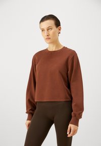 Brauner, kurzer Sweatshirt mit langen Ärmeln und rundem Ausschnitt, mit gerippten Bündchen. Trägt dazu braune, strukturierte Leggings.