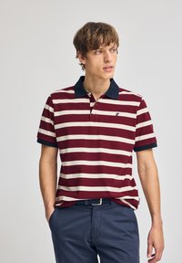 Bordeaux- och krämrandig polotröja med marinblå krage, korta ärmar och en logotyp på bröstet. Tillverkad av bomull, avslappnad passform.