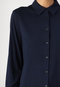 Granatowa koszula zapinana na guziki z kołnierzykiem, długimi rękawami, miękką teksturą i ciemnymi guzikami wzdłuż zapięcia.