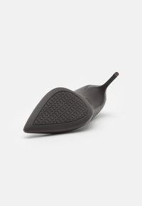Chaussure à talon haut noire avec un bout pointu, en matériau en caoutchouc, semelle texturée présentant un motif étoile et tige élancée au niveau du talon.