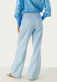 Lichtblauwe wijde spijkerbroek met een denimtextuur, voorzien van achterzakken met knopen en een hoge taille, gecombineerd met een blauwe blouse.